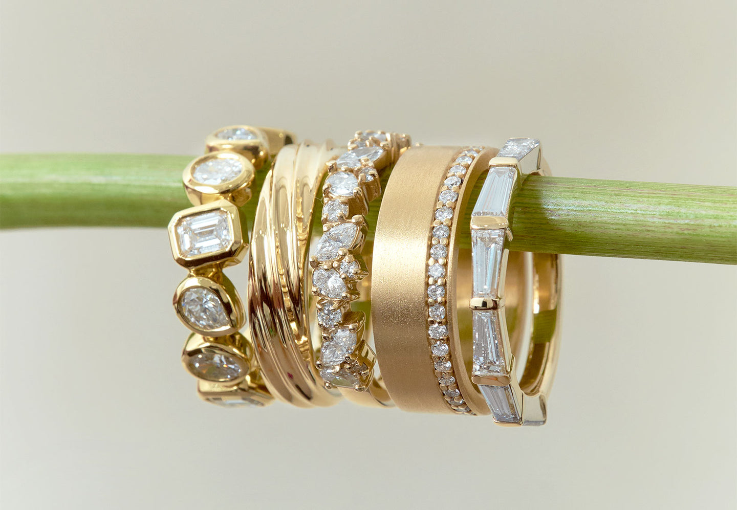 Five mixed style yellow gold and diamond rings hanging from flower stem