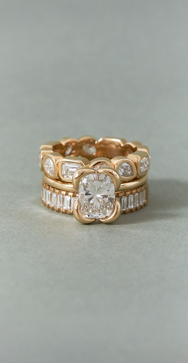 Three yellow gold diamond rings stacked on a light gray-blue surface.