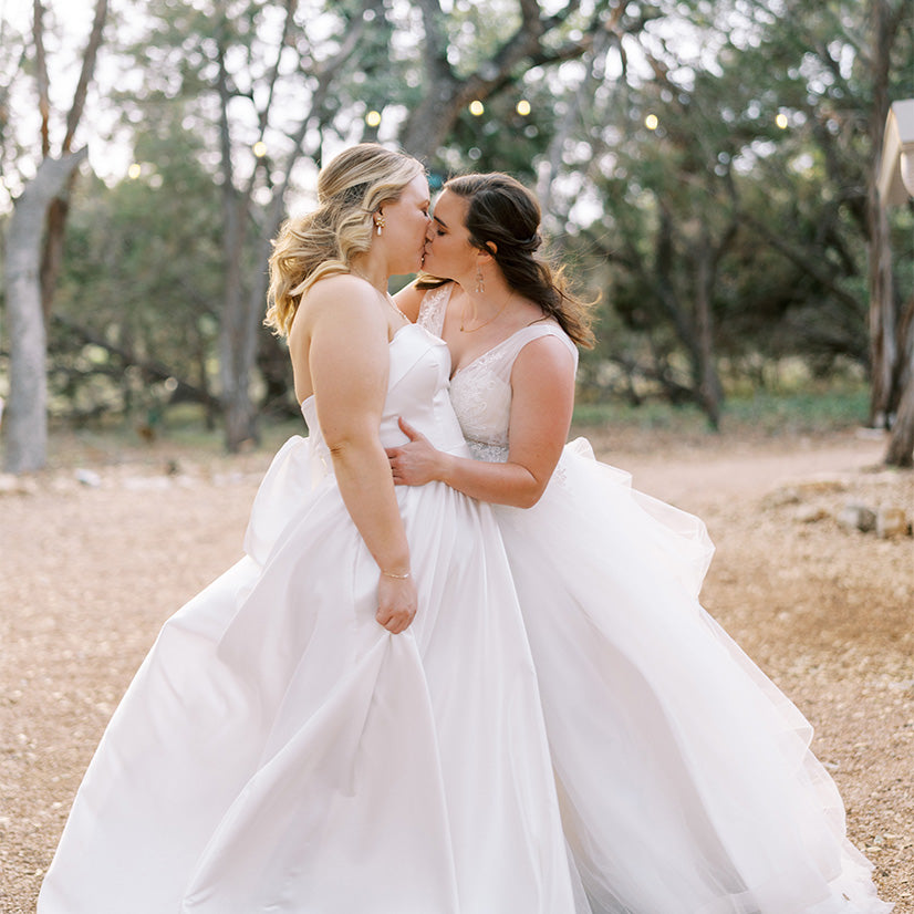 Two brides in white gowns kiss, courtesy of @caitlinrosephoto